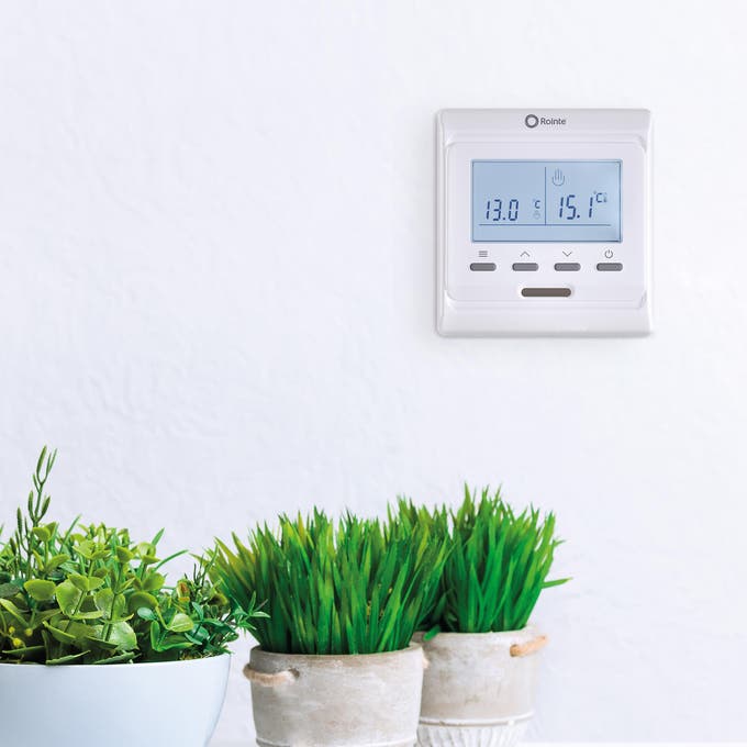 Cronotermostato ROINTE BRANCO instalado numa parede branca e por baixo uma bancada com três vasos de plantas 