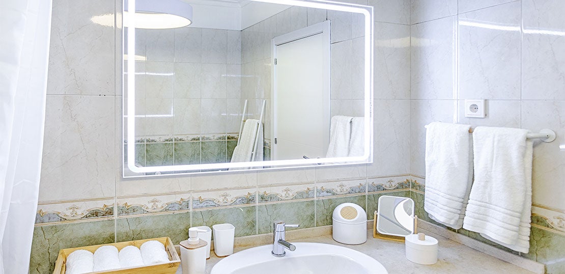 Casa de banho com um espelho com luz e vários acessórios novos