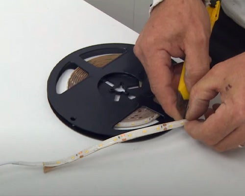 Aplicação das fitas LED em volta do móvel de madeira pintado com tinta branca e o fundo forrado com papel de parede