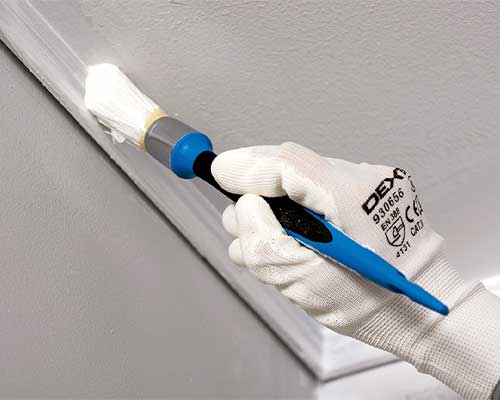 pincel da dexter com tinta branca a pintar a união entre o teto e a parede
