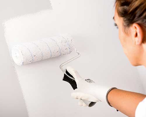 senhora pinta parede de branco com um rolo de pintura.