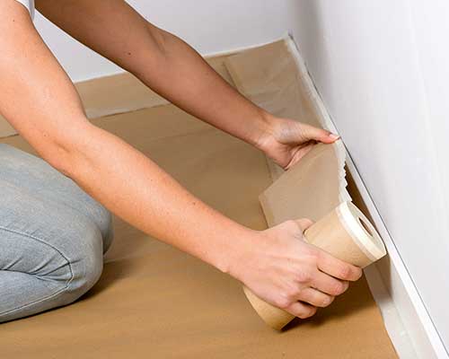 senhora a proteger o chão com fita de pintor antes de começar a pintar a sua parede.