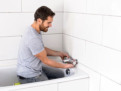 senhor a trocar uma torneira termostática na banheira de uma casa de banho.