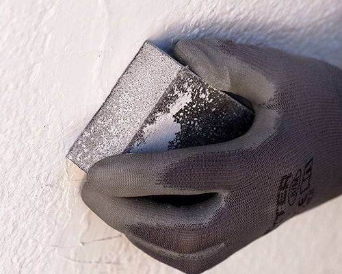 mão com luva de proteção a lixar a parede para a nivelar