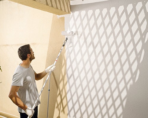 senhor com um cabo de extensão para o rolo a finalizar a pintura no exterior da sua casa 