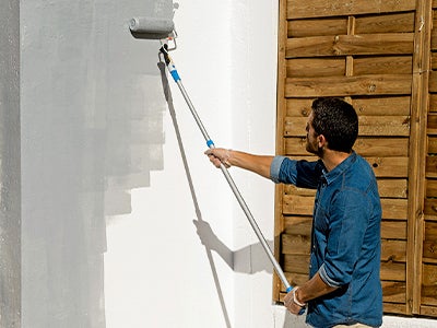senhor a pintar de cinzento uma parede exterior, com o auxílio de um rolo e de um extensor.