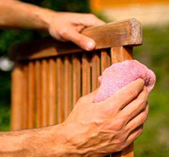mão de senhor a limpar uma cadeira de madeira com um pano cor de rosa