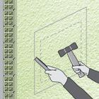 Imagem de uma parede com a marcação das dimensões que um cofre vai ocupar ao ser instalado. Uma mão segura um martelo, outra segura um formão para iniciar a perfuração na parede por forma o cofre poder ser instalado
