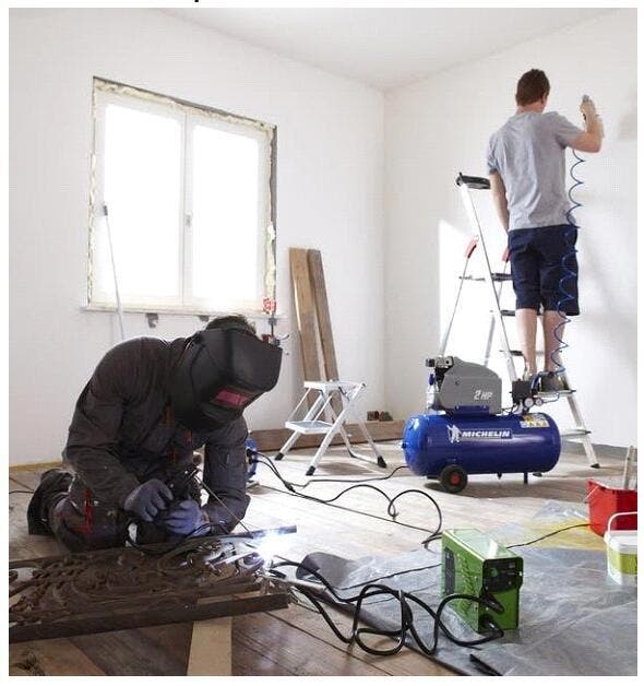 local de uma obra no interior de um quarto com uma janela em que um compressor está a ser utilizado para pintar uma parede com o auxílio de uma pistola de tinta em spray