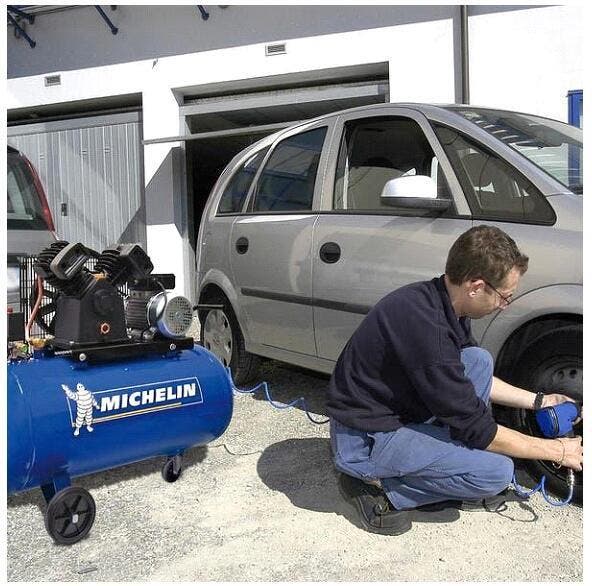 um mecânico está a utilizar o compressor de ar michelin para encher o pneu de um carro