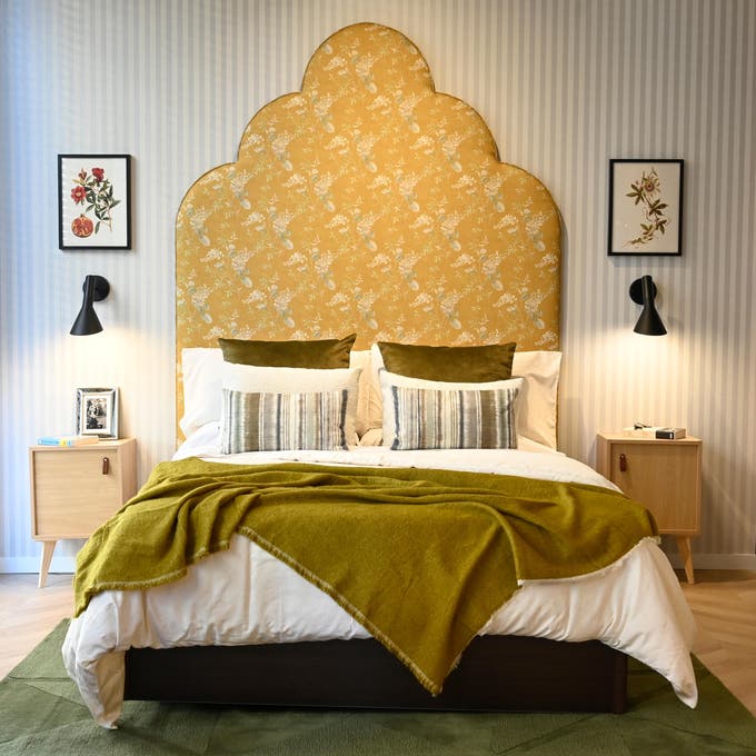Dormitorio con papel pintado de rayas y gran cabecero tapizado. 