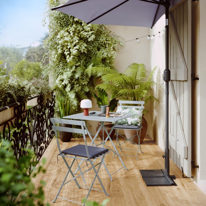 cenário de jardim com mesa quadrada e duas cadeiras azuis, além de guarda-chuva e material vegetal