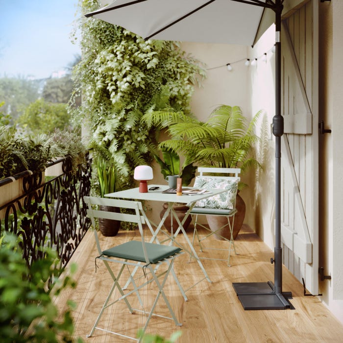 cenário de jardim com mesa quadrada e duas cadeiras verdes, além de guarda-chuva e material vegetal