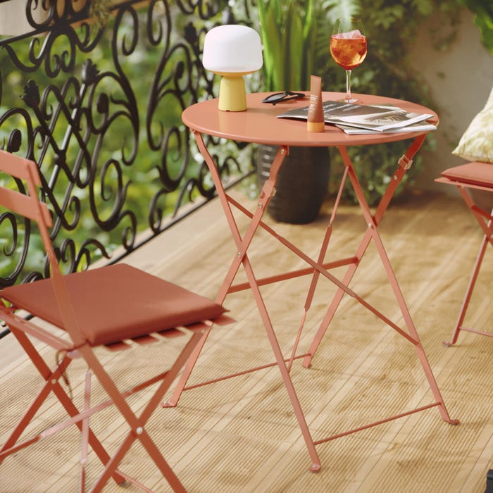 uma mesa de jardim para 2 pessoas com 2 cadeiras laranja, material floral
