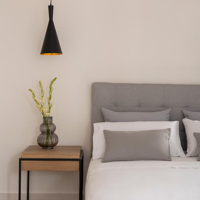 quarto com parede branca, cabeceira cinza e mesa de cabeceira de madeira e ferro 