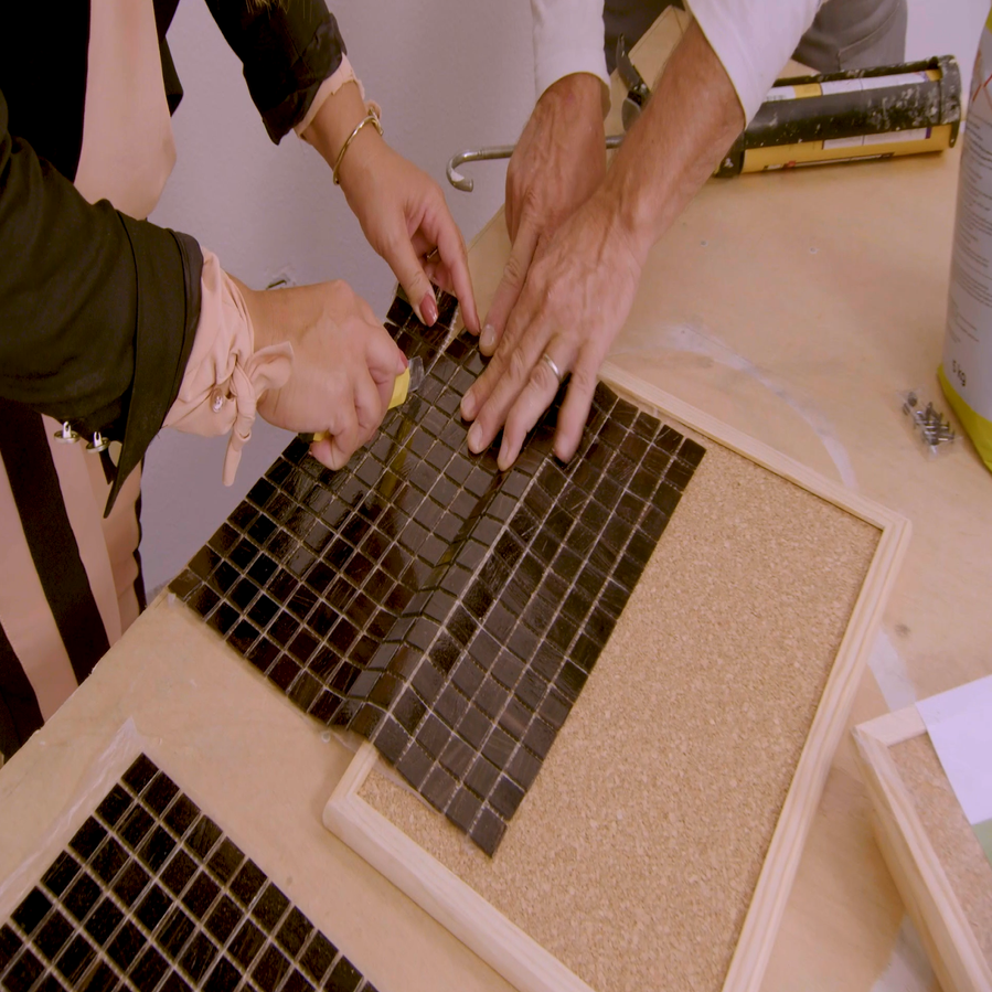 duas pessoas a cortar a pastilha cerâmica na dimensão do quadro de cortiça