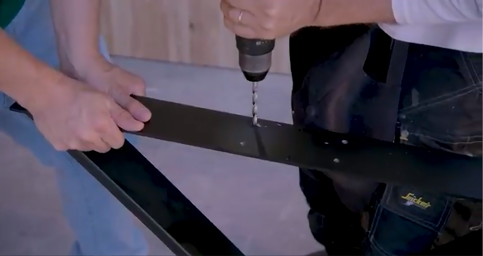 duas pessoas a fazer um novo furo nos pés da mesa com um berbequim