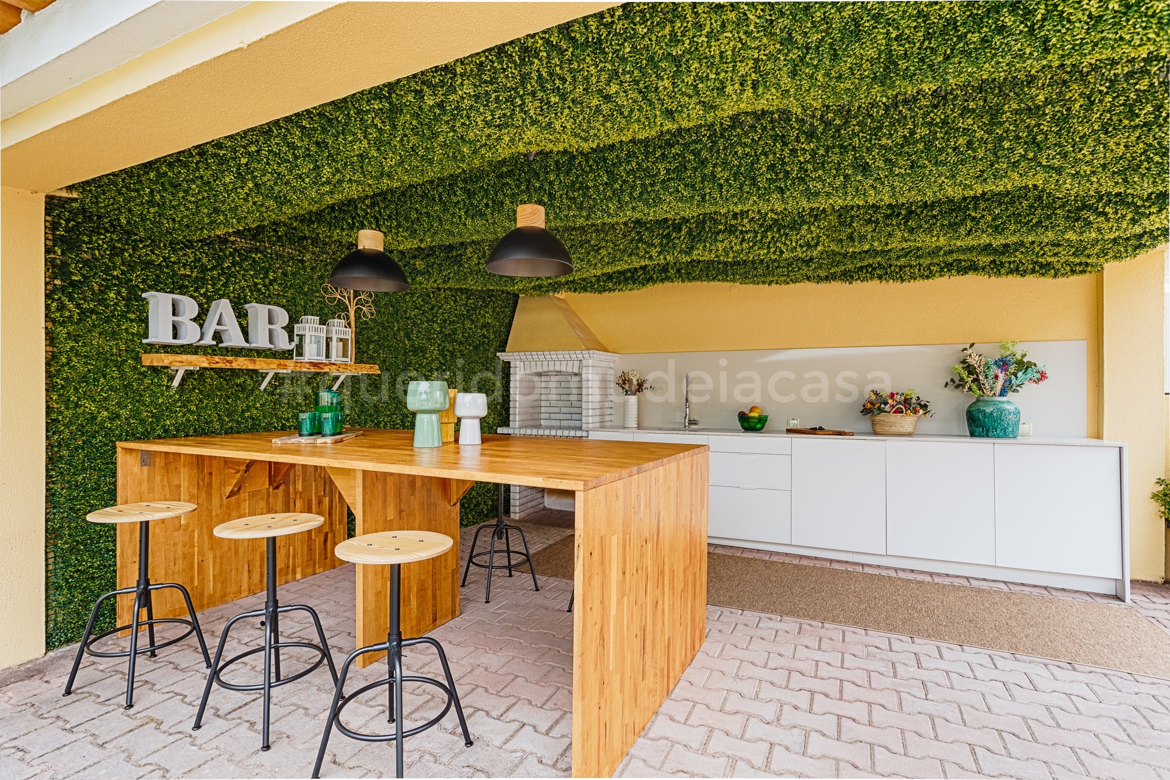 mesa alta de bar em madeira junto a uma cozinha de exterior debaixo de um jardim vertical