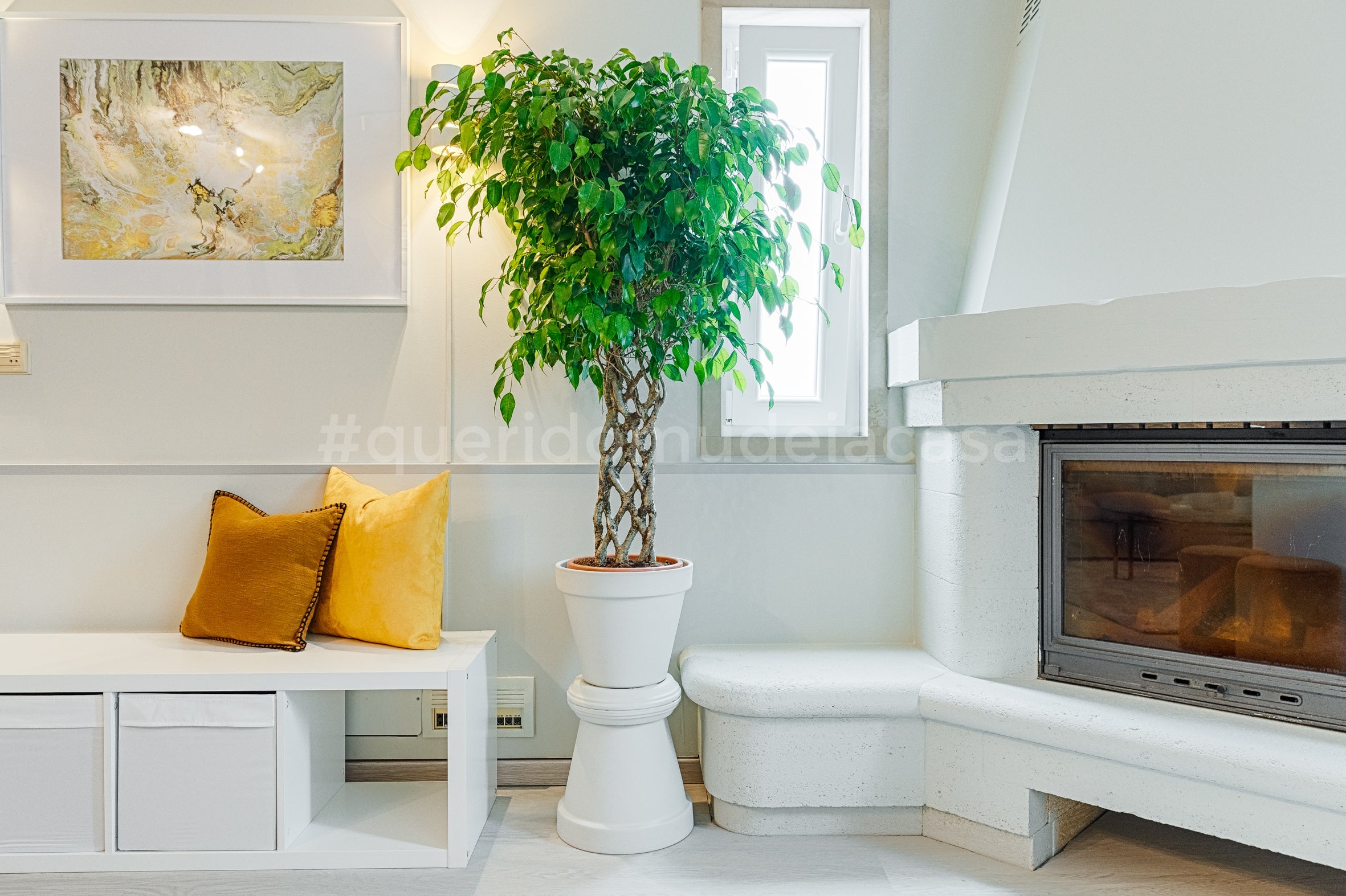 Sala elegante em tons de branco com apontamentos coloridos como almofadas e um vaso de barro pintado de branco