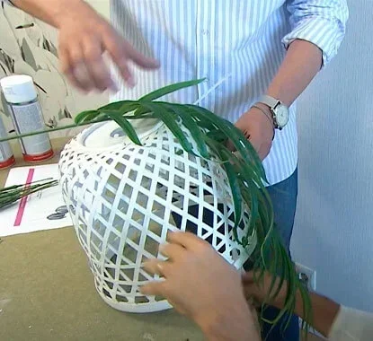 Senhor a fixar as folhas de uma planta artificial num abajur de palhinha com abraçadeiras