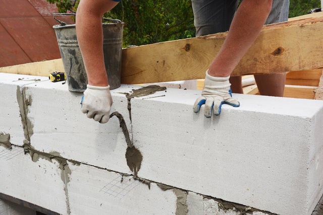 Ręce mężczyzny pokrywające beton komórkowy, obok stoi metalowe wiadro