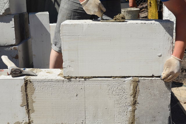 Mężczyzna murujący beton komórkowy, obok leży siekiera