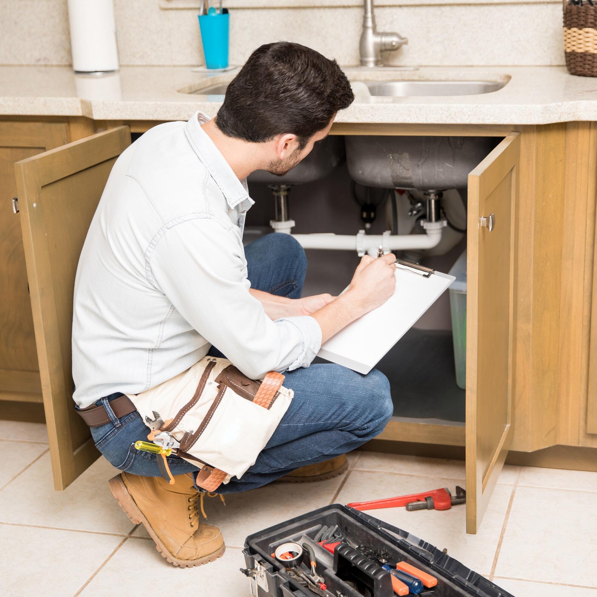 Hydraulik sprawdza instalację pod zlewem kuchennym.