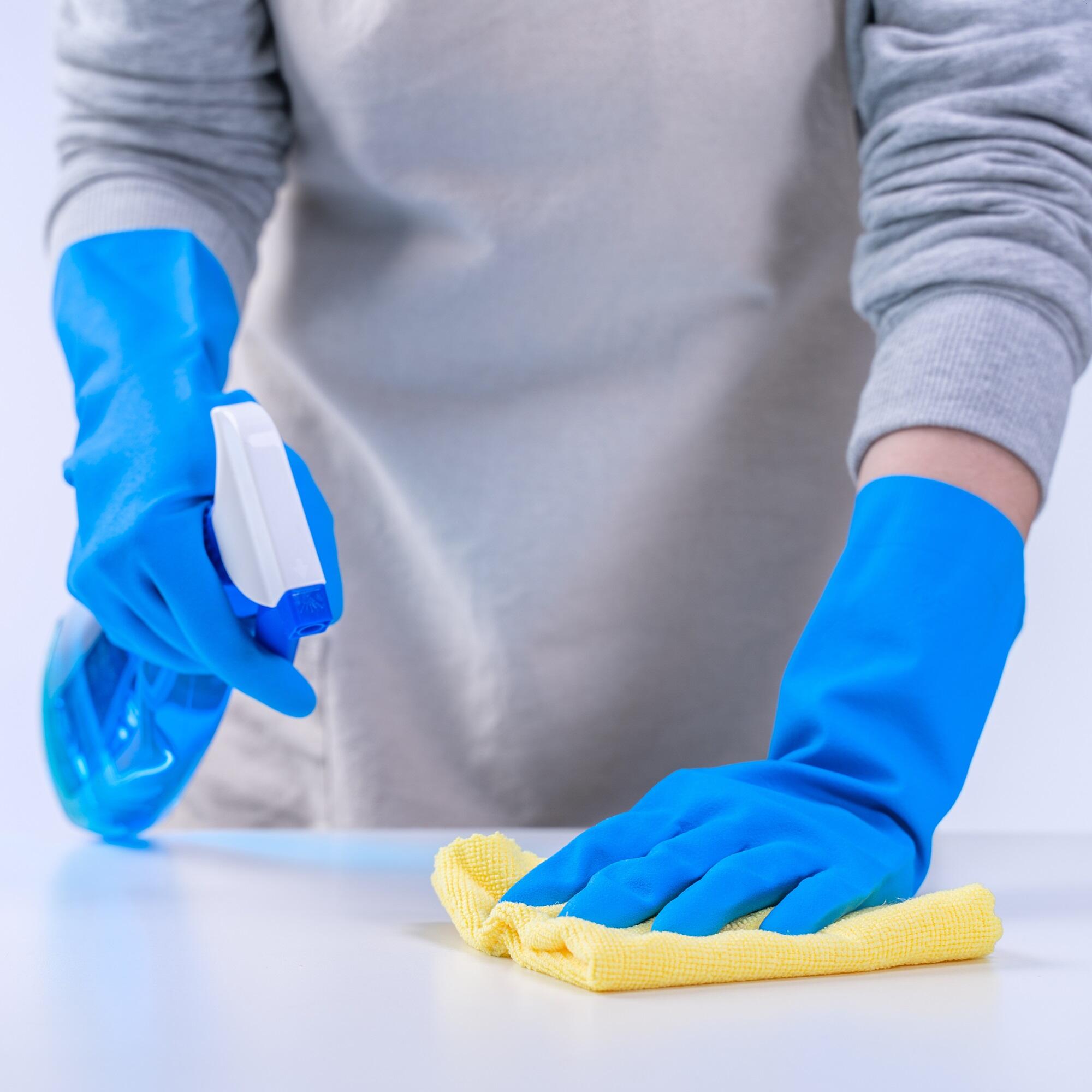 Czyszczenie blatu żółtą ściereczką i środkiem w sprayu w niebieskich rękawicach.