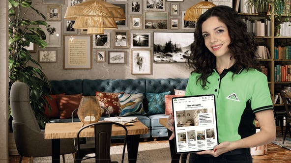 Ambiente molto decorativo con tanti prodotti differenti e in evidenza ragazza con divisa leroy merlin che mostra su un tablet una pagina del sito