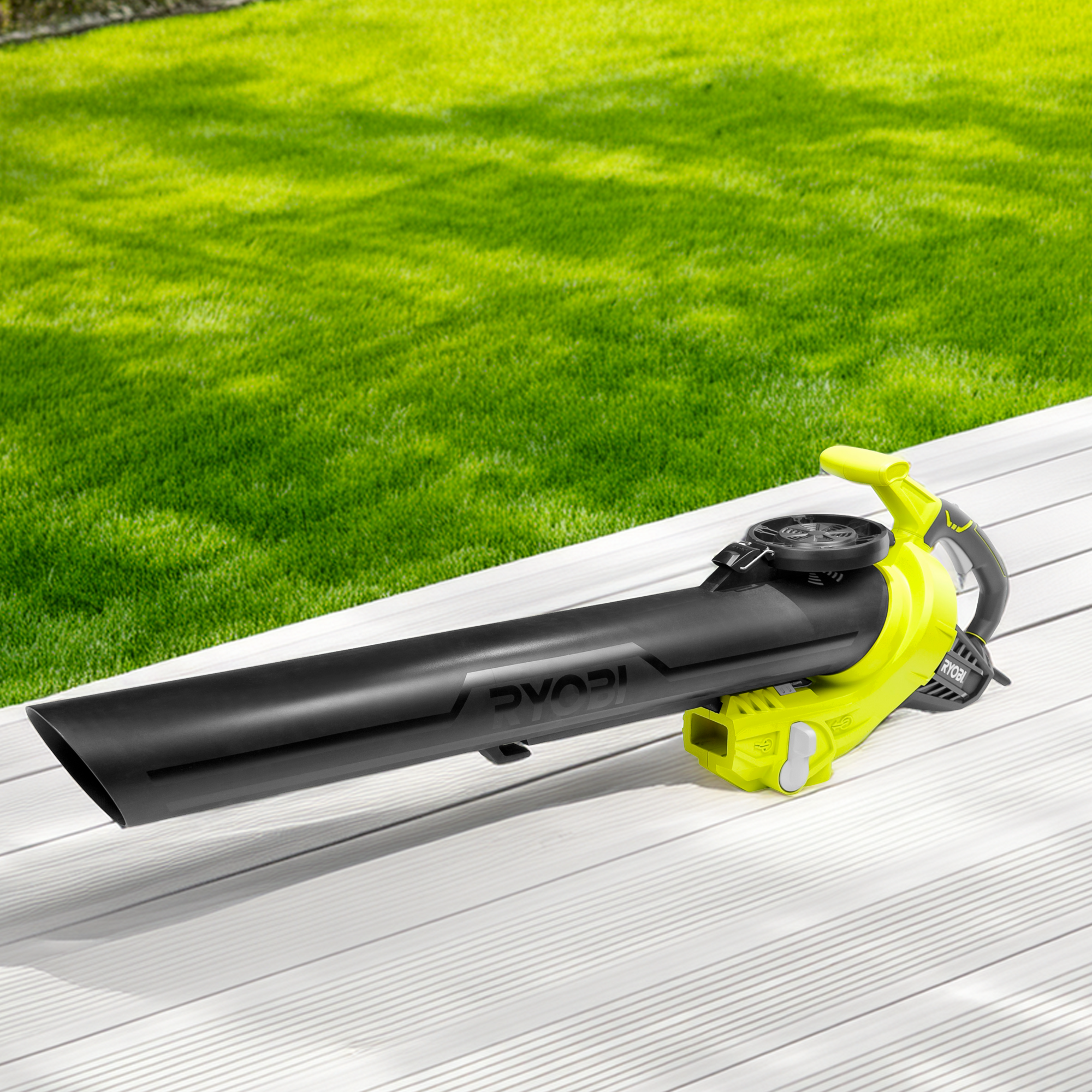 Odkurzacz z dmuchawą Ryobi RBV3000CESV 3000W leży na białym tarasie przy trawniku.