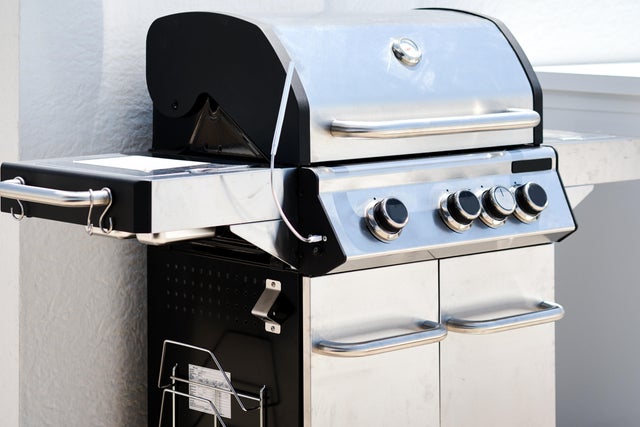 Stalowy grill ogrodowy z bocznymi półkami i szafkami na dole.