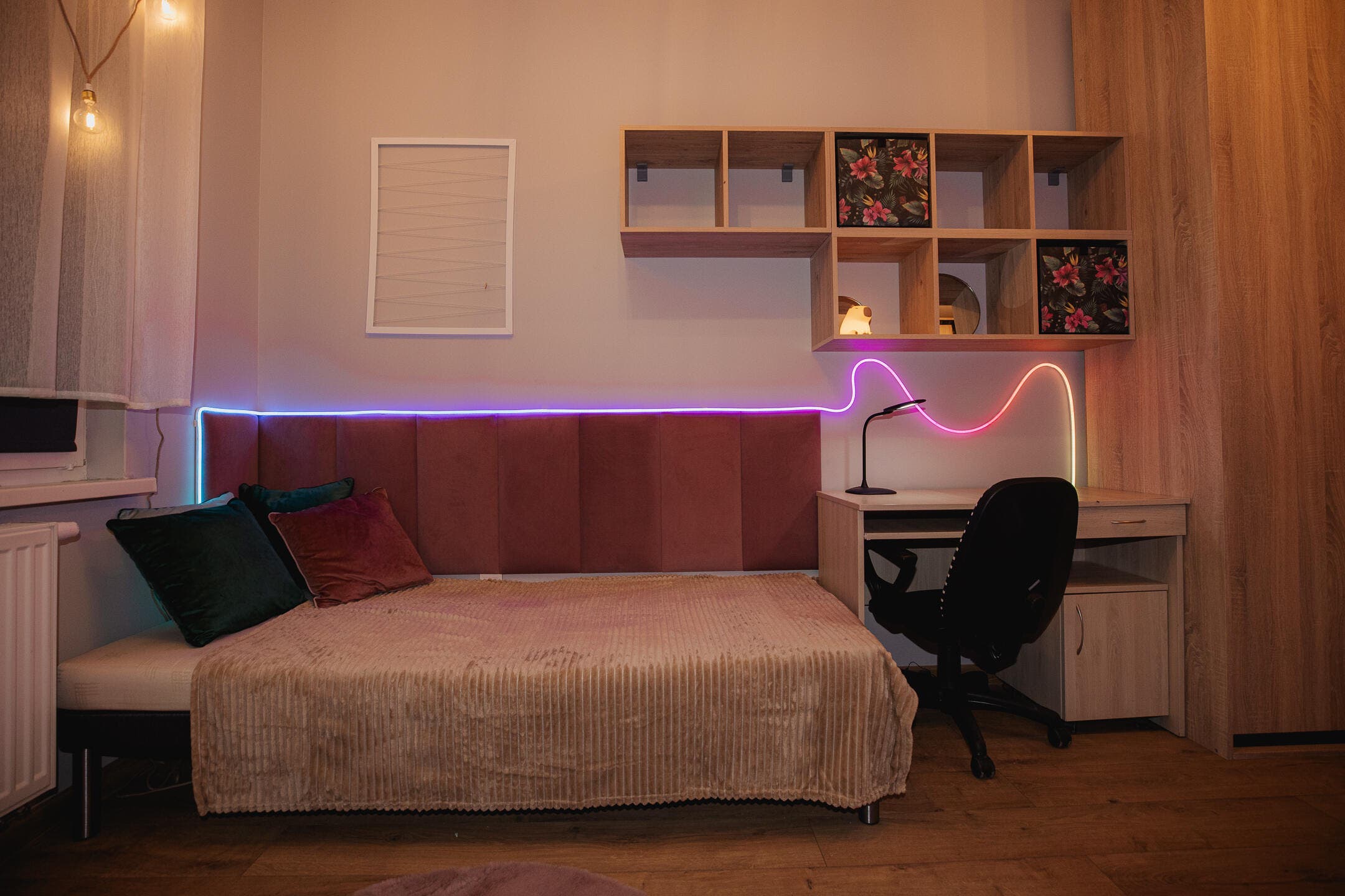 zdjęcie wyremontowanego pokoju; na zdjęciu widać część pokoju przy oknie z łóżkiem pojedynczym, na ścianie przy łóżku są panele naścienne, powyżej na ścianie półki. Na zdjęciu również jest biuro z krzesłem obrotowym