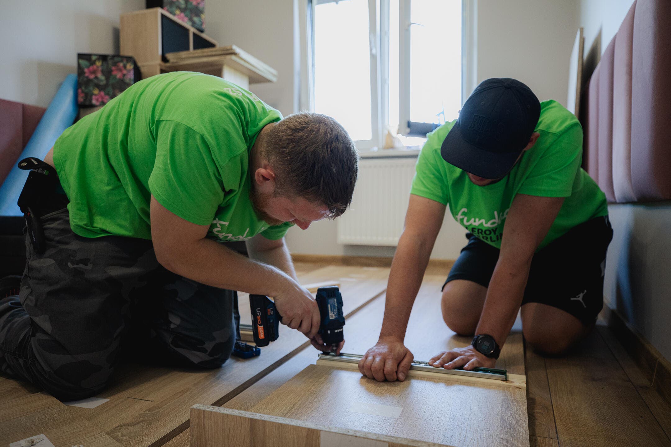 dwóch wolontariuszy skręca części szafy na podłodze