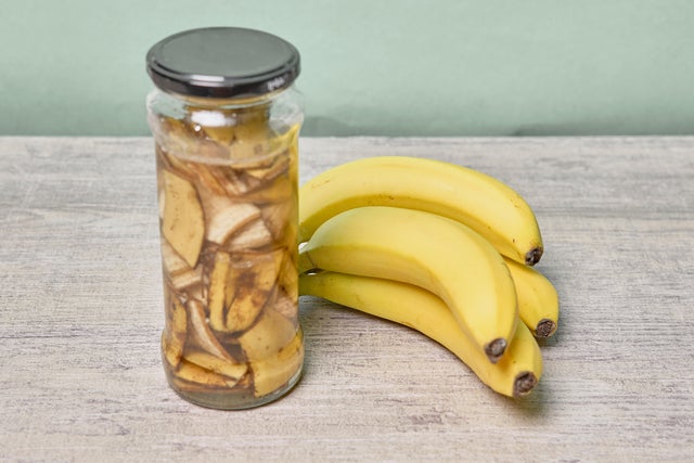 Słoik z domowym nawozem bananowym obok kiści świeżych bananów na drewnianym blacie.
