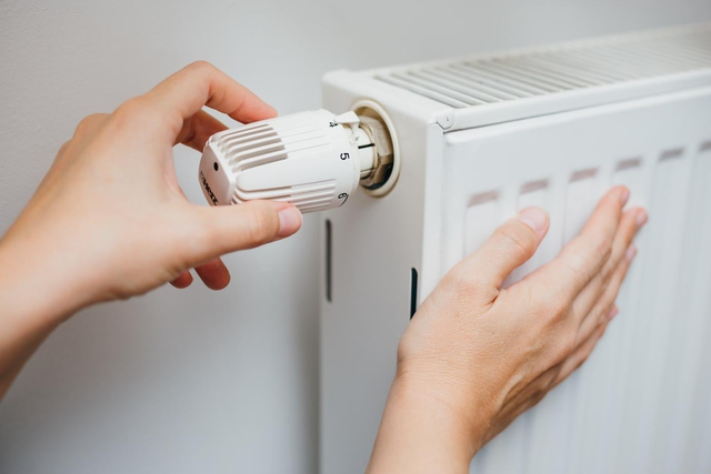 Regulacja termostatu na grzejniku ręką.