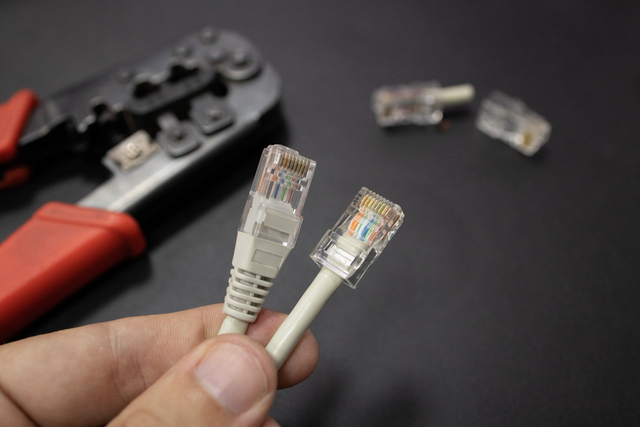 Dwie końcówki kabla sieciowego RJ45 trzymane w dłoni obok zaciskarki do kabli.