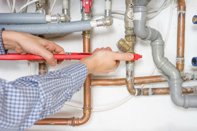 Hydraulik w koszuli w kratę dokręca mosiężny zawór na miedzianej rurze za pomocą czerwonego klucza nastawnego.