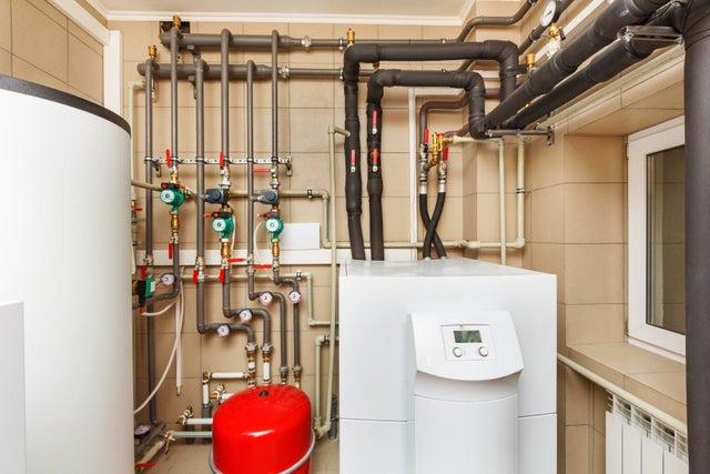 Kotłownia z pompą ciepła, zasobnikiem ciepłej wody i rozbudowaną instalacją rurową z pompami obiegowymi.
