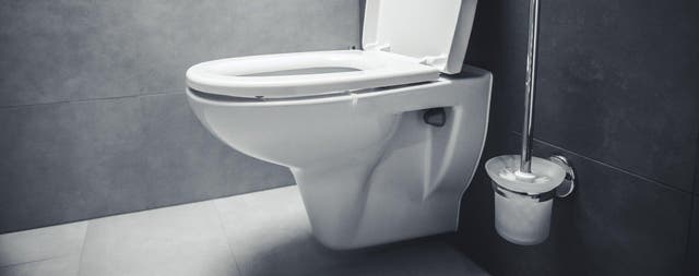 Toaleta podwieszana z otwartą deską sedesową i szczotką WC w łazience z ciemnoszarymi płytkami.