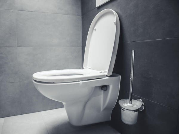 Toaleta podwieszana z otwartą deską sedesową i szczotką WC w łazience z ciemnoszarymi płytkami.