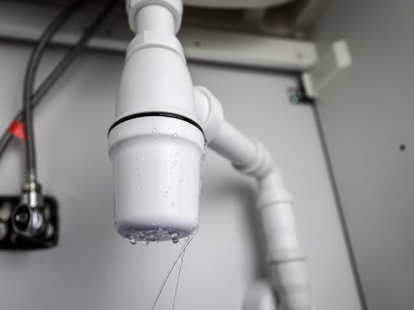 Nieszczelny syfon plastikowy pod zlewem kuchennym z cieknącą wodą z uszkodzonego złącza rury kanalizacyjnej.