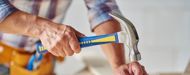 Cieśla wbijający gwóźdź młotkiem w drewnianą deskę podczas prac stolarskich na budowie.