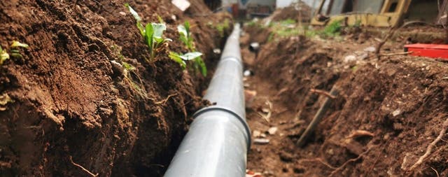 Szara rura kanalizacyjna PVC ułożona w wykopie ziemnym podczas budowy zewnętrznej instalacji odpływowej lub wodociągowej.