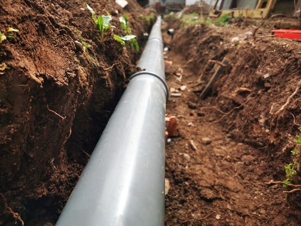 Szara rura kanalizacyjna PVC ułożona w wykopie ziemnym podczas budowy zewnętrznej instalacji odpływowej lub wodociągowej.