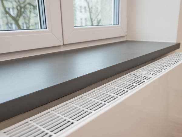 Szary parapet wewnętrzny zamontowany nad białym grzejnikiem pod oknem PVC.