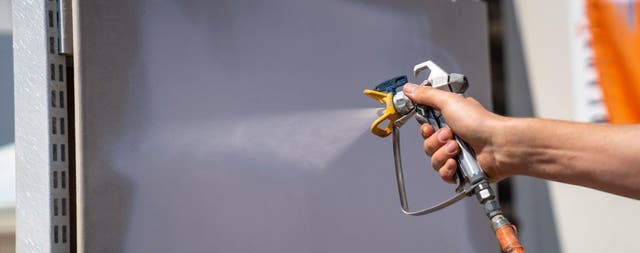 Natryskowe malowanie płyty elewacyjnej profesjonalnym pistoletem bezpowietrznym podczas prac budowlanych.