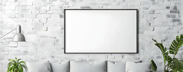 Nowoczesny salon w stylu loft z szarą sofą, roślinami dekoracyjnymi i pustą ramą na ścianie z malowanego kamienia dekoracyjnego.