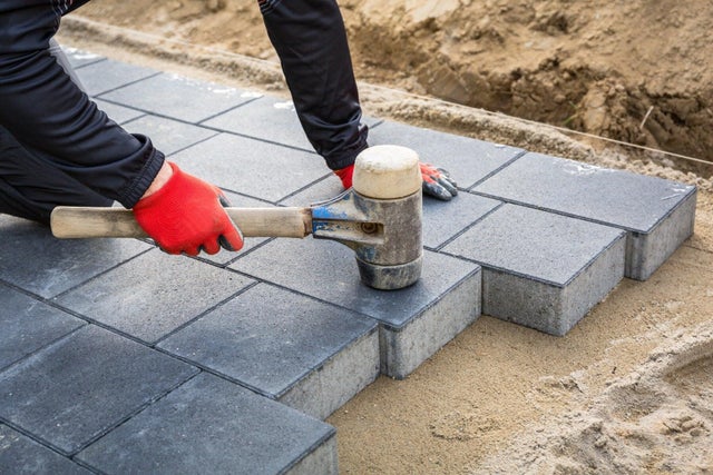 Układanie ciemnoszarej kostki brukowej betonowej młotkiem gumowym na podsypce piaskowej.