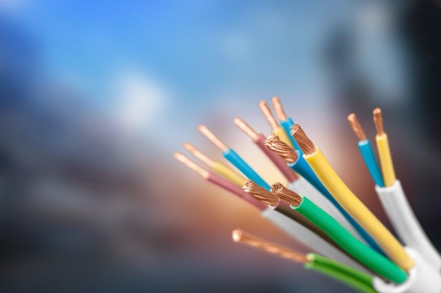 Zbliżenie na oголone miedziane końcówki wielożyłowych przewodów elektrycznych w kolorowych izolacjach na niebieskim tle.