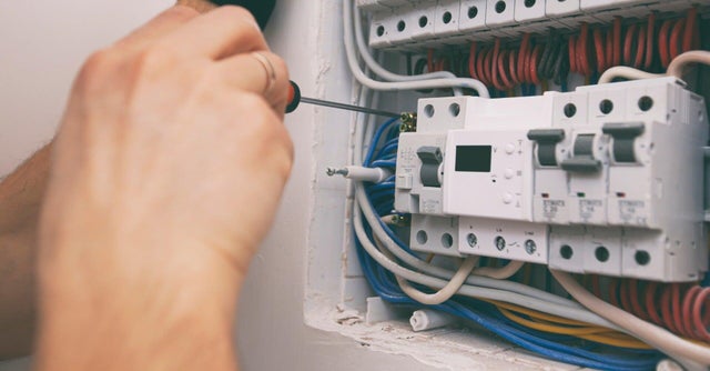 Elektryk dokręcający śrubokrętem zaciski wyłącznika różnicowoprądowego w skrzynce rozdzielczej z wieloma kolorowymi przewodami.